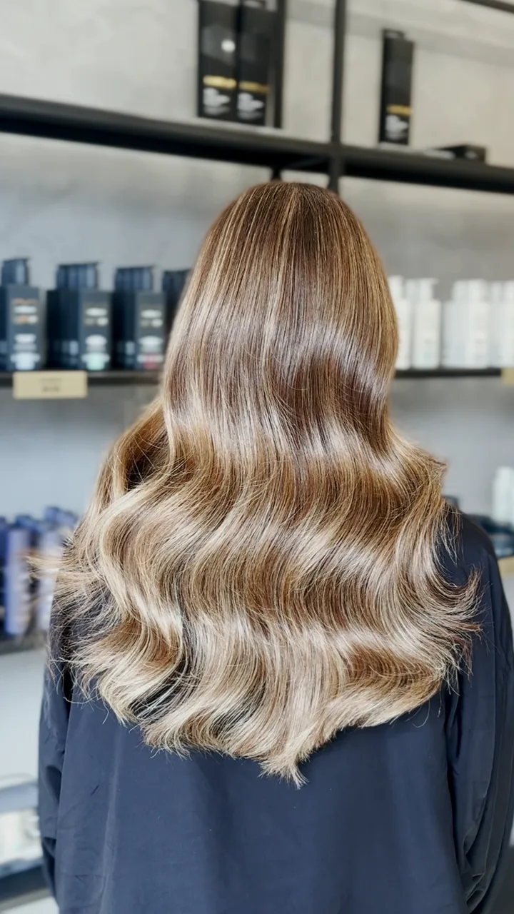 Long blonde hair before and after a soft balayage, finished in glossy waves